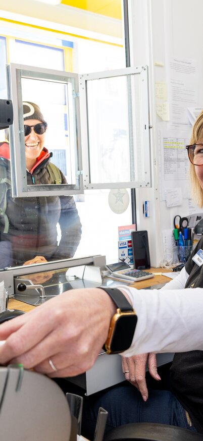 Eine lächelnde Kassenmitarbeiterin übergibt einem Gast ein Ticket an der Kassa der Dachstein-Gletscherbahn. | © Harald Steiner