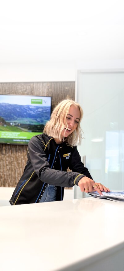 Info & Service – Wir sind gerne für dich da! | © Hauser Kaibling Freundliche Mitarbeiterin am Hauser Kaibling berät Gäste mit einem Lächeln. | © Hauser Kaibling