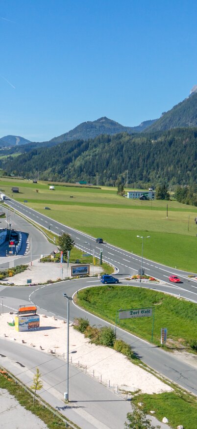 Luftaufnahme der Talstation Hauser Kaibling mit großem Parkplatz, Straßenanbindung und Bergpanorama im Hintergrund. | © Baumgartner