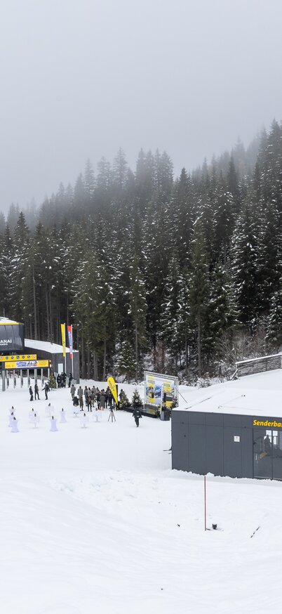 Schneebedeckte Berglandschaft mit der neuen 10er-Gondelbahn Senderbahn Hauser Kaibling und der 8er-Sesselbahn Mitterhausalm I. Menschen versammeln sich zur offiziellen Eröffnung der 4-Berge Ski Super Connection, umgeben von Wald und Nebel. | © Martin Huber