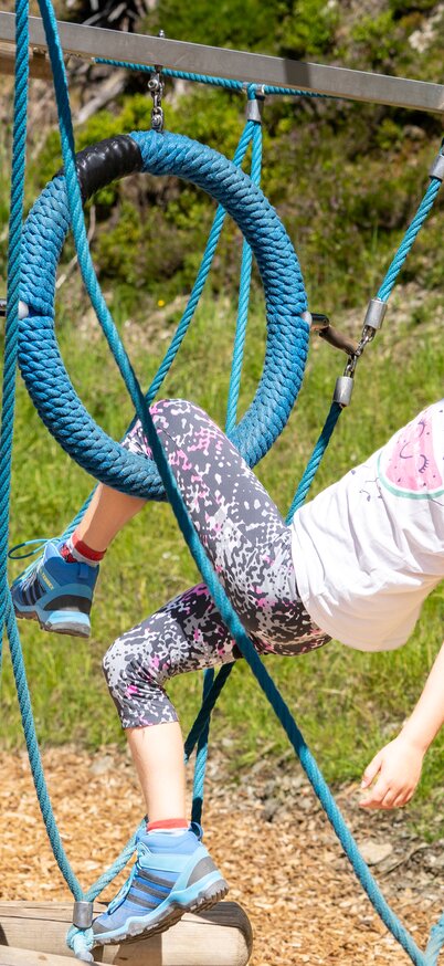 Ein Mädchen klettert lachend durch ein Kletterseil-Element im Spielparcours von Wollis Bergabenteuer am Hauser Kaibling. | © Josh Absenger
