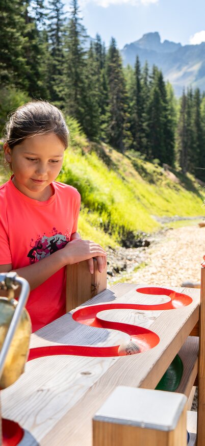 Children explore Wollis' wooden marble run in Hauser Kaibling in the Dachstein Tauern, surrounded by mountains and alpine meadows. | © Josh Absenger