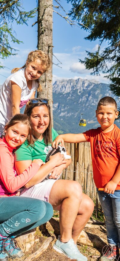 Eine Familie mit Kindern sitzt im Schatten und hält einen kleinen Hasen im Arm, gemeinsam beim Streichelzoo. | © Josh Absenger