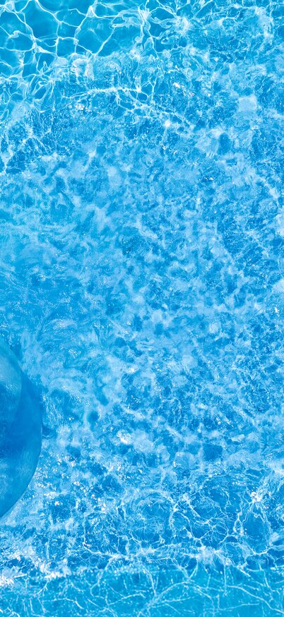 Blick von oben auf eine Person, die in einer transparenten Zorbing-Kugel über die Wasseroberfläche läuft, das blaue Wasser funkelt in der Sonne. | © Josh Absenger