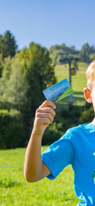A child is standing in an alpine meadow, holding the Schladming-Dachstein Card | © René Eduard Perhab