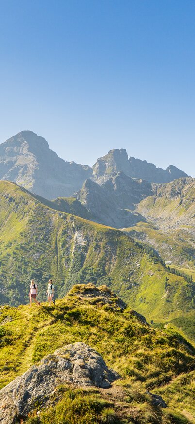 Zwei Frauen stehen auf einem Bergrücken am Hauser Kaibling in der Region Schladming-Dachstein, mit grandiosem Rundblick auf die umliegenden Gipfel. | © Josh Absenger