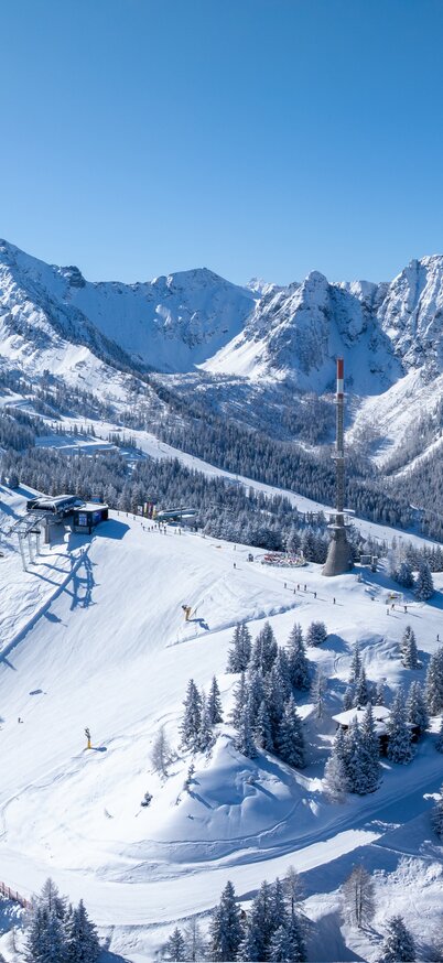 Drohnenaufnahme vom Senderplateau mit verschneiten Pisten, urigen Skihütten und den imposanten Gipfeln der Schladminger Tauern im Hintergrund. | © Josh Absenger