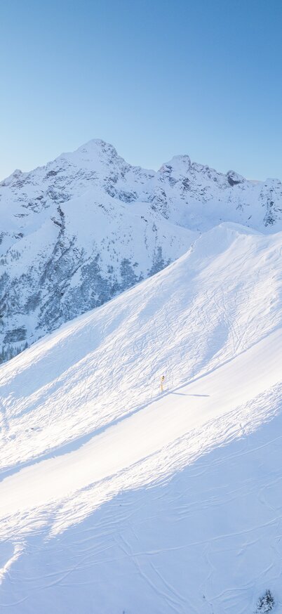 Verschneiter Gipfel des Hauser Kaibling im Morgenlicht mit Sonne, die hinter den Bergen aufgeht. | © Josh Absenger
