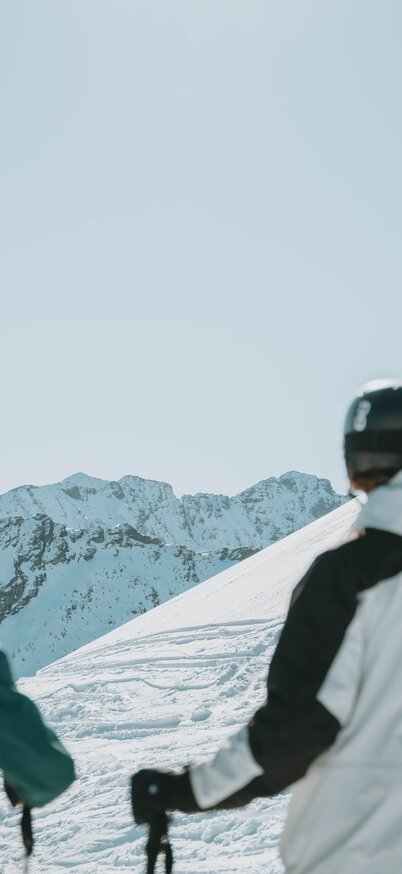 Drei Skifahrer mit Helmen und Skistöcken blicken von der Skipiste am Hauser Kaibling auf die umliegenden verschneiten Berge. | © Robin Betzel