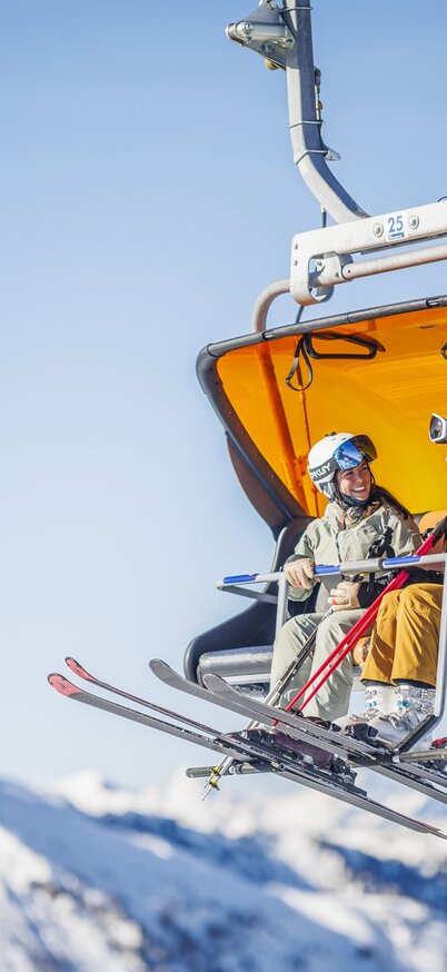 Zwei Skifahrerinnen genießen die Fahrt mit dem Sessellift vor der verschneiten Bergkulisse am Hauser Kaibling. | © Anry_LUKAC