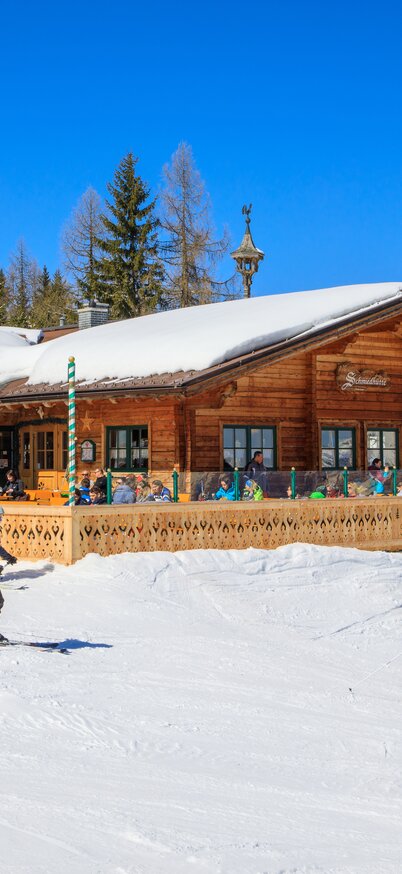 Skifahrer vor der Schmiedhütte am Hauser Kaibling an einem sonnigen Wintertag mit klarer Bergkulisse. | © Hauser Kaibling