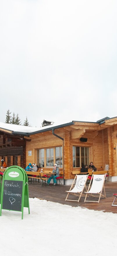 Exterior view of the Stöcklhütte in winter with deckchairs and sunny terrace, snowy landscape in the foreground. | © Hauser Kaibling