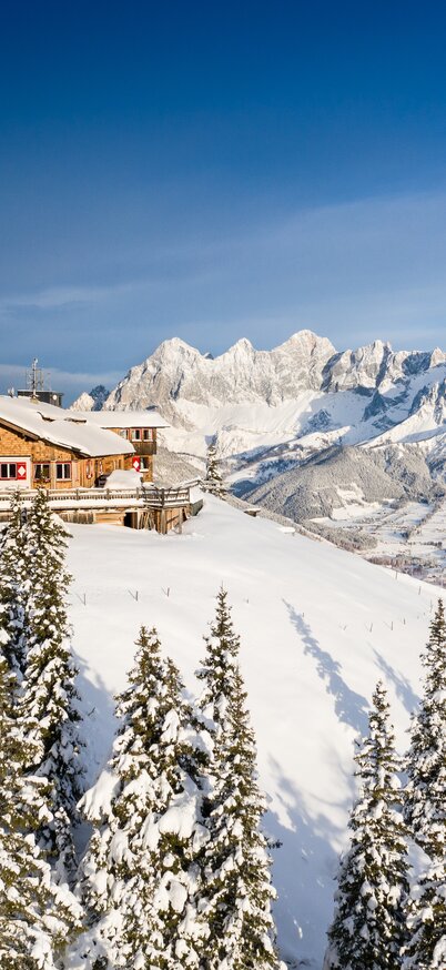 Zwei Skifahrer an der Hochwurzen, mit verschneiter Hütte und Dachsteinblick im Hintergrund | © Josh Absenger