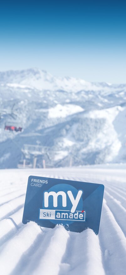 my Ski amadé Friends Card steckt im frisch präparierten Piste vor verschneiter Alpenkulisse | © Claudia Ziegler