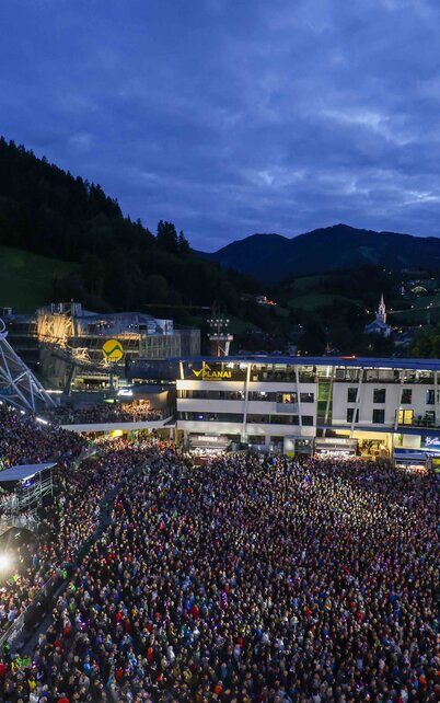 Thousands of visitors fill Planai Stadium during the Schladming-Dachstein Summer Opening. The spectator areas and the surroundings of the Planai valley station can be seen in the evening atmosphere. | ©  Daniel Scharinger