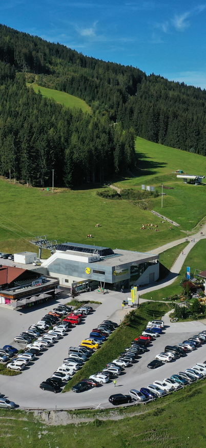 Sommerliche Ansicht der Talstation der Gipfelbahn Hochwurzen mit Parkplätzen und grünen Wiesen | © Max Kollau