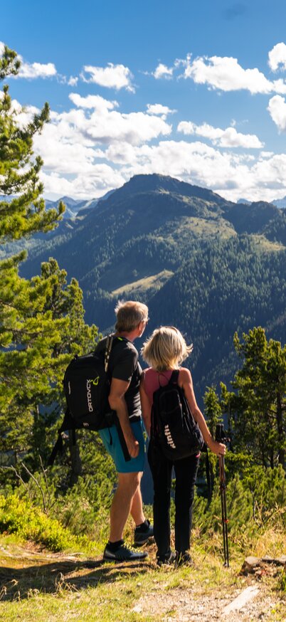 Zwei Wandernde stehen mit Rucksack am Aussichtspunkt und blicken ins weite Bergpanorama der Hochwurzen | © Christine Höflehner
