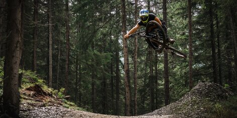 Downhiller zeigt Trick in der Luft auf der 99 Jumpline im Bikepark Schladming im Wald | © Henrieke Ibing