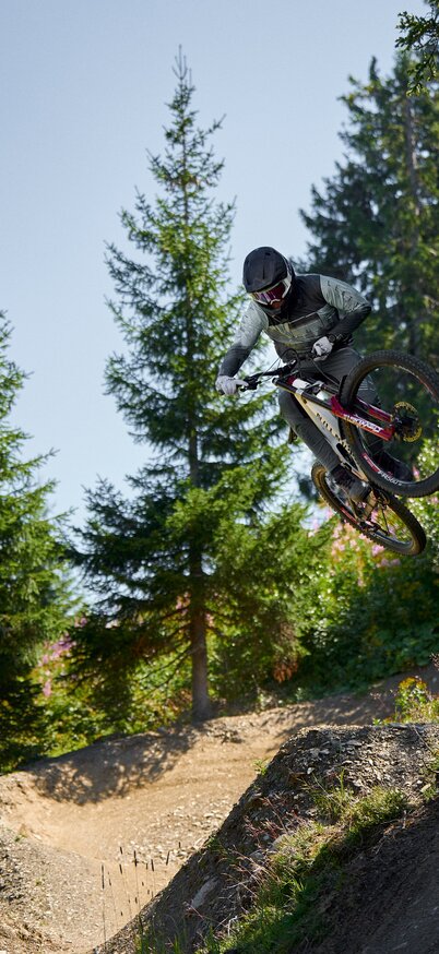 Ein Biker springt mit voller Schräglage auf der Pro Downhill Strecke durch den Wald im Bikepark Schladming | © Dietmar Koerbler