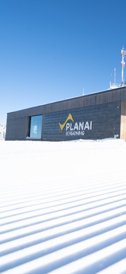 Blick auf die Planai Bergstation bei strahlendem Sonnenschein und frisch präparierter Skipiste | © Josh Absenger