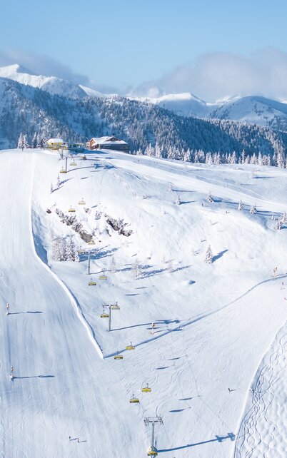Schneebedeckte Mitterhausalm II mit Sessellift und präparierten Pisten im Skigebiet Planai | © Josh Absenger