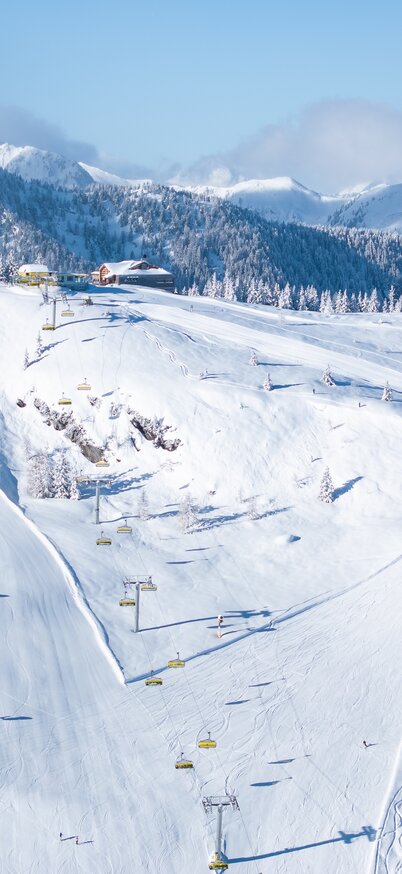 Luftaufnahme der Mitterhausalm II mit Skipisten im Winterpanorama | © Josh Absenger Schneebedeckte Mitterhausalm II mit Sessellift und präparierten Pisten im Skigebiet Planai | © Josh Absenger