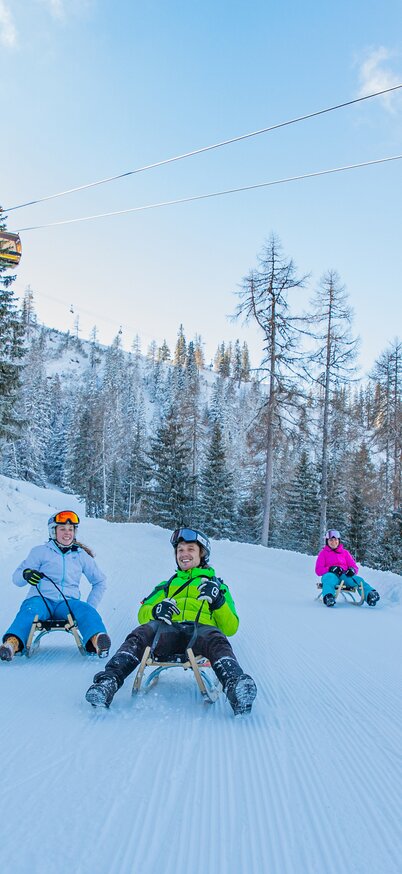 Rodeln auf der Hochwurzen und im Hintergrund die Gipfelbahn Hochwurzen | © René Eduard Perhab