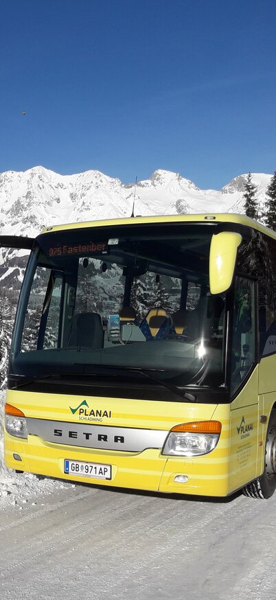 Planai-Skibus mit Blick auf das verschneite Dachsteinmassiv | © Planai Bahnen Planai-Bus auf schneebedeckter Straße mit Blick auf das Dachsteinmassiv bei strahlendem Sonnenschein | © Planai Bahnen