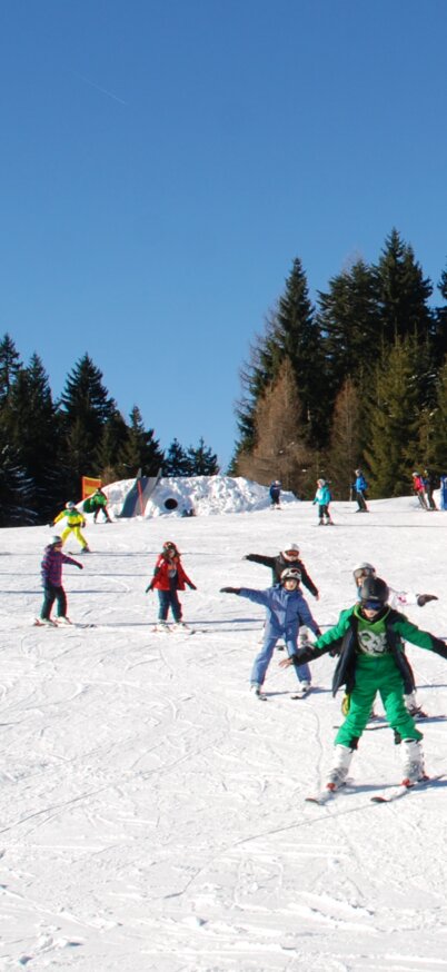 Skikurskinder fahren neben dem Zauberteppich im Kinderland Reiteralm mit den SKiern runtern. | © Reiteralm Bergbahnen