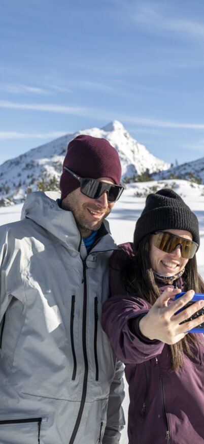 Ein Pärchen steht im Schnee auf der Reiteralm und macht ein Selfie. | © Lorenz Masser