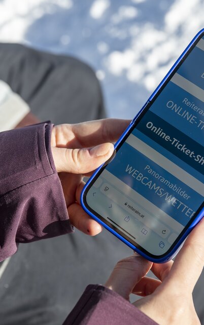 Ein Frau hält ein Handy in der Hand und hat die Homepage der Reiteralm geöffnet. | © Lorenz Masser