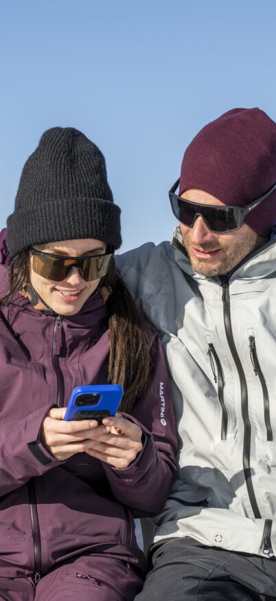 Ein Paar sitzt auf dem Reiteralm-Schriftzug vom Steirerherz auf der Gasselhöhe und schaut ins Handy. | © Lorenz Masser