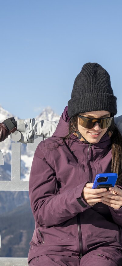 Ein Paar sitzt auf dem Reiteralm-Schriftzug vom Steirerherz auf der Gasselhöhe und schaut ins Handy. | © Lorenz Masser