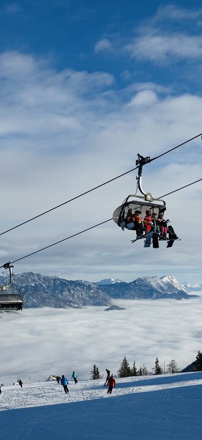 Es sitzen Leute in einem Sessel des Lifts auf der Reiteralm. Unterhalb fahren Gästen die Piste hinunter | © Reiteralm Bergbahnen