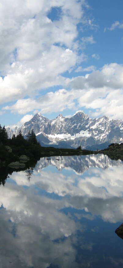 Spiegelsee auf der Reiteralm mit Spiegelung vom Dachstein Dreigestein und wunderschöner Aussicht auf die Berge.