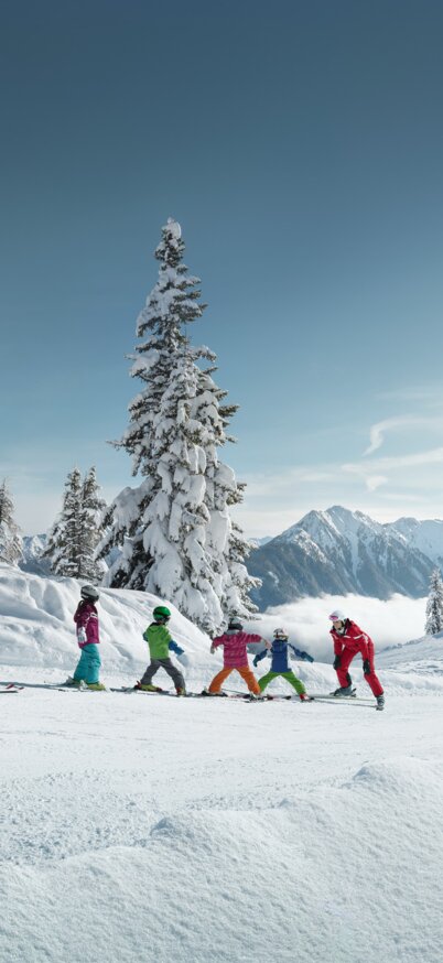 Kinder fahren einem Skilehrer nach umgeben von einer traumhaften Bergwelt | © Peter Burgstaller