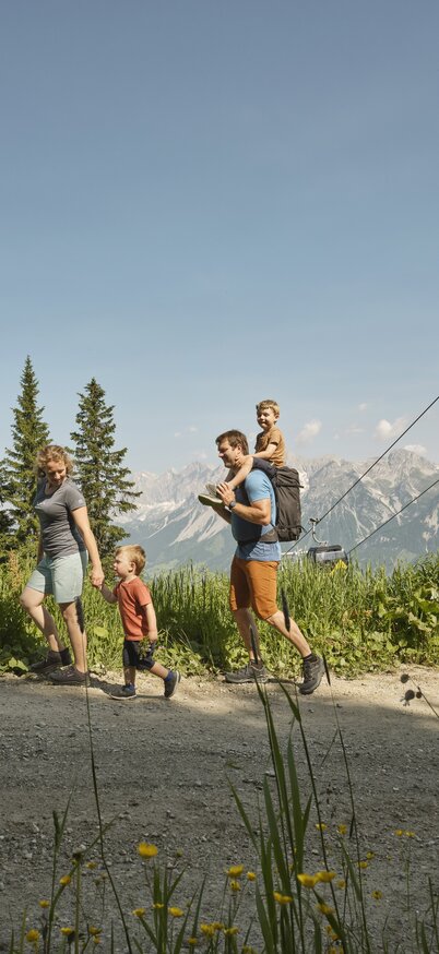 Familie wandert auf der Planai auf einem Schotterweg, im Hintergrund die Planai Seilbahn. | © Peter Burgstaller