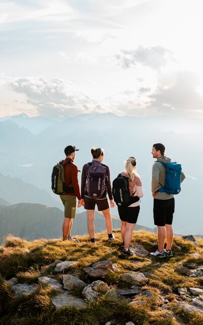 Vier Personen stehen auf einem Gipfel und schauen in die Weite, im Hintergrund sieht man weite Berglandschaft | © Mathäus Gartner