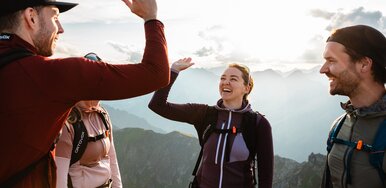 Vier Personen sind wandern, zwei davon klatschen miteinander ein, im Hintergrund sieht man weite Berglandschaft | © Mathäus Gartner