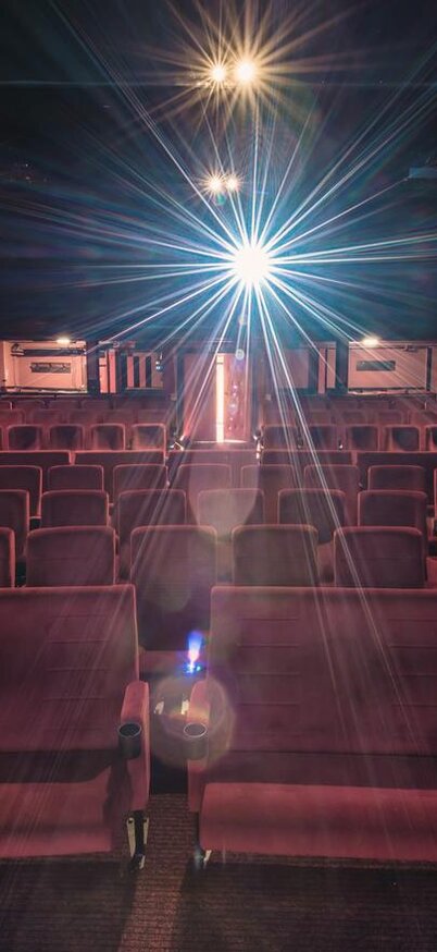 Ein leerer Kinosaal mit rot gefütterten Sitzen. Ein Projektor strahlt Licht auf die Leinwand. | © Christoph HUBER